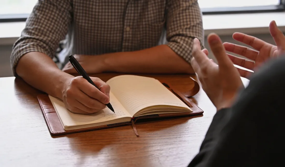 Une personne prend des notes à la main dans un carnet pendant une discussion